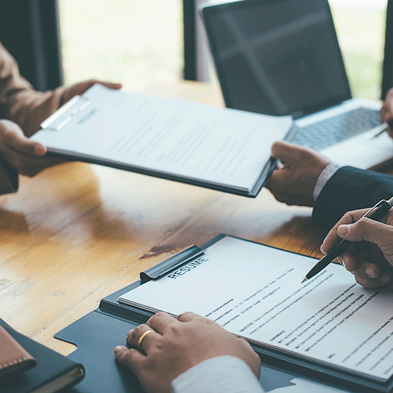 Business meeting with people reviewing resumes and documents at a table with a laptop